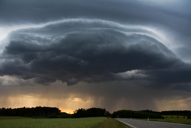 Picture of a very large, black cloud--basically a thunderstorm--dropping a lot of rain over a highway and fields. 