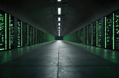 An image of the inside of a data center. It's dark with a black floor. There are banks of computers lit up in green on both sides of the floor.