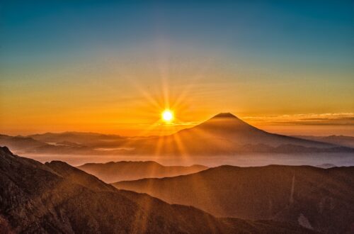 Sun over Mt. Fuji, Japan. The sky is blue, and just above the mountains is a band of orange and yellow.