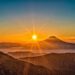 Sun over Mt. Fuji, Japan. The sky is blue, and just above the mountains is a band of orange and yellow.