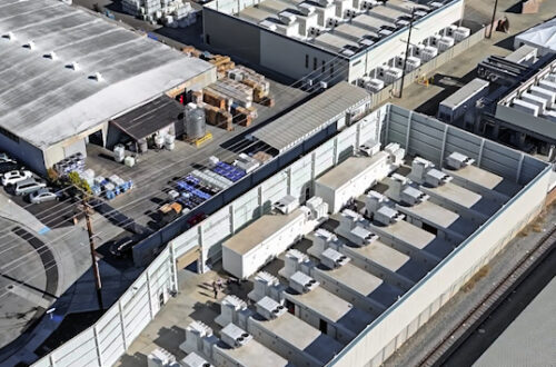 An image of a modular battery storage facility in California. It looks like a series of lined-up white, rectangular containers.