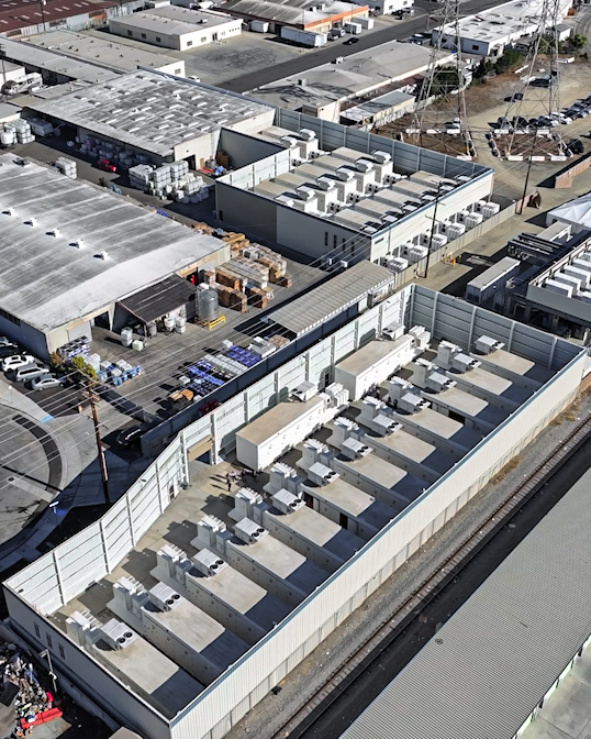 An image of a modular battery storage facility in California. It looks like a series of lined-up white, rectangular containers.