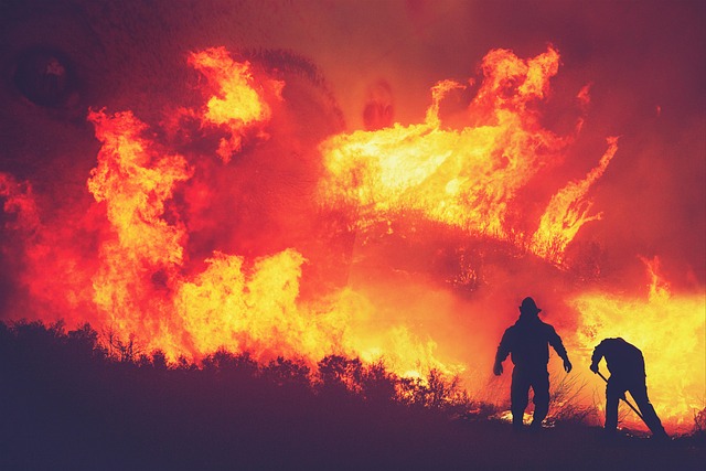 A photo of two firefighters on a hill fighting a wall of huge flames.
