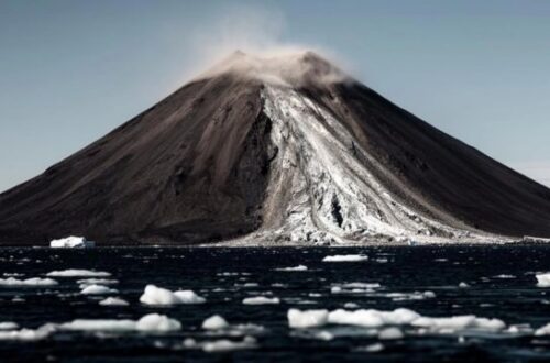 A photo of a volcanic island showing a landslide of rock and ice pouring down the face.