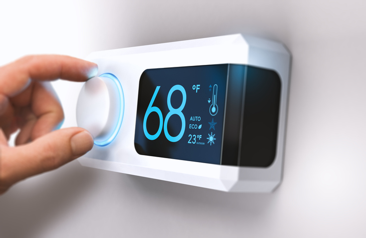 A digital thermostat set to 68 degrees Fahrenheit with fingers on the control knob.